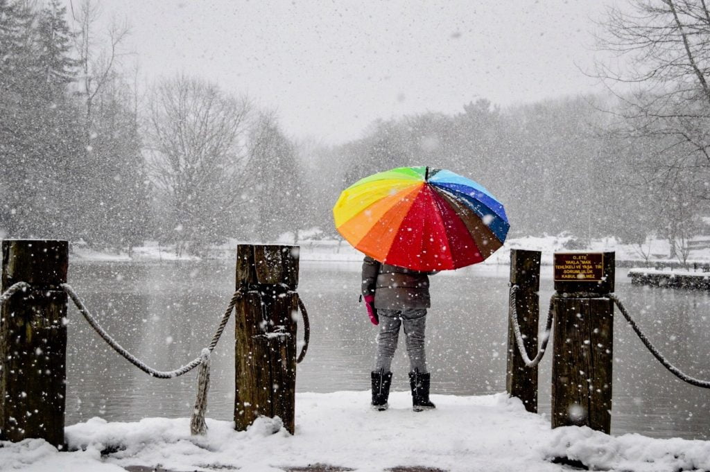 Coping by sheltering from snow under a rainbow-coloured umbrella