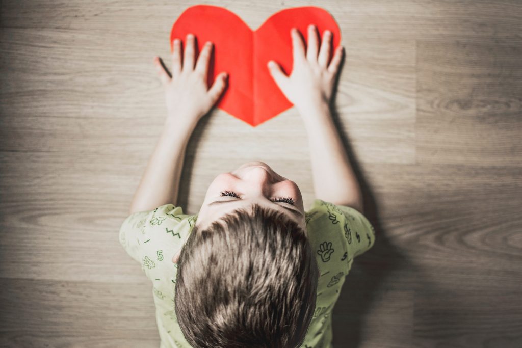 Child with heart-shaped paper cutout, representing trusting relationship