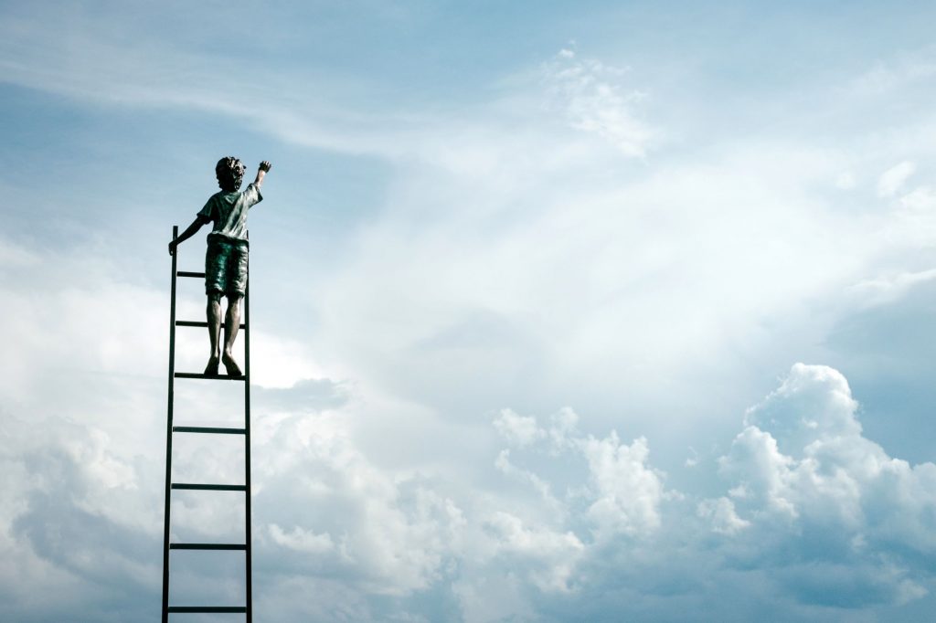 Boy on ladder stretching for the sky, representing growth